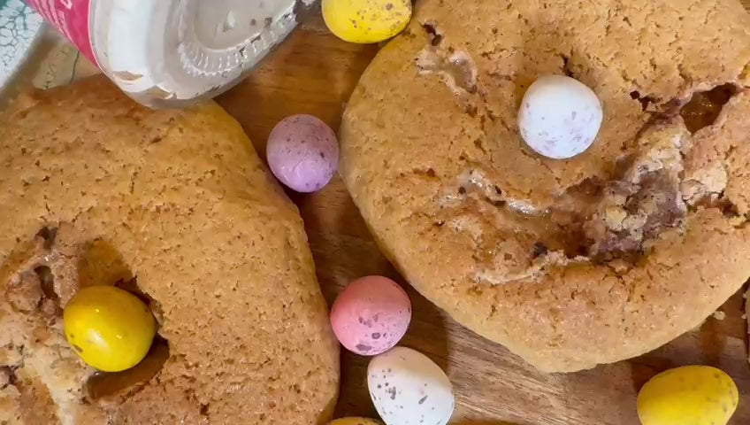 Mini Egg cookies stuffed with Mini Egg Butter, topped with pastel chocolate mini eggs and broken open to reveal a gooey chocolate centre.