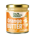 Glass jar of The Yorkshire Kitchen Orange Butter with a gold metal lid and bright orange label. The label features the brand name at the top and large white text reading ‘Orange Butter,’ alongside an illustration of a sliced orange. Additional text reads ‘Decadently creamy with a Cointreau infusion’ and ‘Smear on a teacake’ and ‘Melt on a warm brownie.