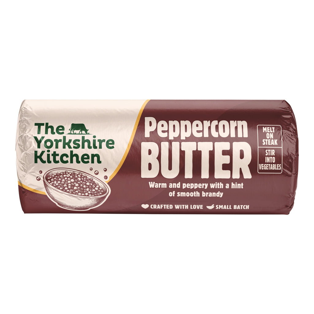 Wrapped roll of The Yorkshire Kitchen Peppercorn Butter in deep brown and cream packaging, featuring an illustration of a bowl of peppercorns. Large white text reads ‘Peppercorn Butter’ with the description ‘Warm and peppery with a hint of smooth brandy.’ The wrapper suggests ‘Melt on steak’ and ‘Stir into vegetables,’ and includes ‘Crafted with love’ and ‘Small batch’ text.