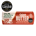 Wrapped roll of The Yorkshire Kitchen Cajun Butter in red and cream packaging, featuring illustrations of chillies, garlic, and spices. Large white text reads ‘Cajun Butter’ with the description ‘Punchy flavour with a gentle warmth.’ The wrapper suggests ‘Stir through pasta’ and ‘Baste chicken,’ and displays Great Taste award badges including 2025.