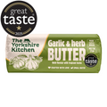 Wrapped roll of The Yorkshire Kitchen Garlic & Herb Butter in green and cream packaging, featuring illustrations of garlic bulbs and herbs. Large white text reads ‘Garlic & Herb Butter’ with the description ‘Bold flavour with fragrant herbs.’ The wrapper also suggests ‘Make garlic bread’ and ‘Melt on steak.’ Great Taste 2025 award badges appear on the packaging.